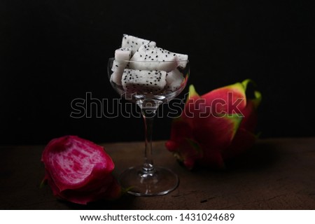 A piece of Dragon fruit in wine glass with whole and some slice, fruit in the glass, dark food photography