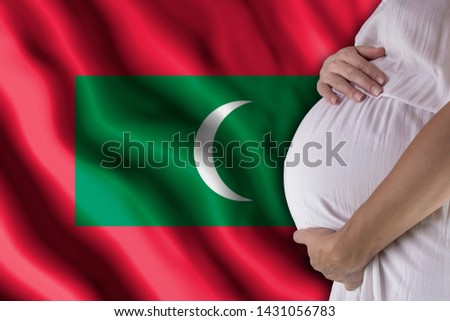 Conditions of birth of the child, the childbirth allowance, state support for young mothers, a pregnant girl holds her hands on the stomach close-up against the background of the flag of Maldives
