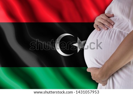 Conditions of birth of the child, the childbirth allowance, state support for young mothers, a pregnant girl holds her hands on the stomach close-up against the background of the flag of Libya