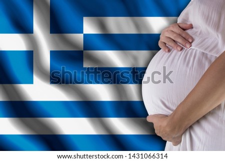 Conditions of birth of the child, the childbirth allowance, state support for young mothers, a pregnant girl holds her hands on the stomach close-up against the background of the flag of Greece