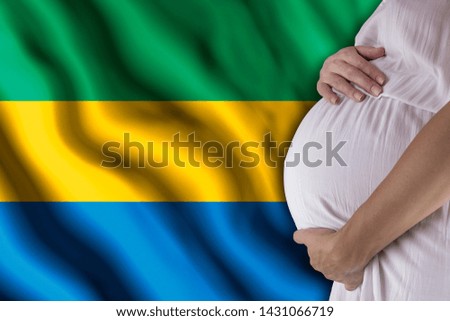 Conditions of birth of the child, the childbirth allowance, state support for young mothers, a pregnant girl holds her hands on the stomach close-up against the background of the flag of Gabon