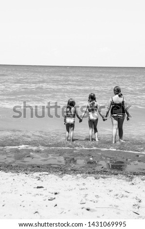 back view of three sisters holding hands walking into beach water black and white