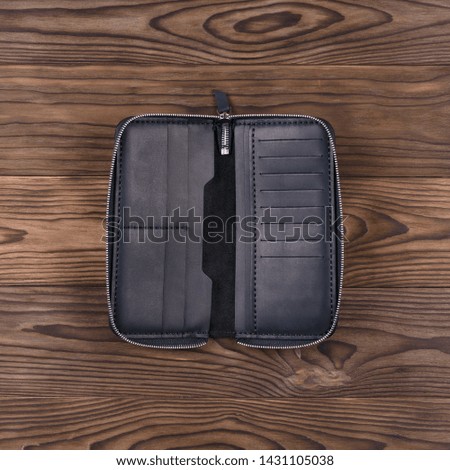 Mattle black color handmade leather porte-monnaie on wooden textured background. Oper purse. Up to down view. Stock photo of luxury accessories.