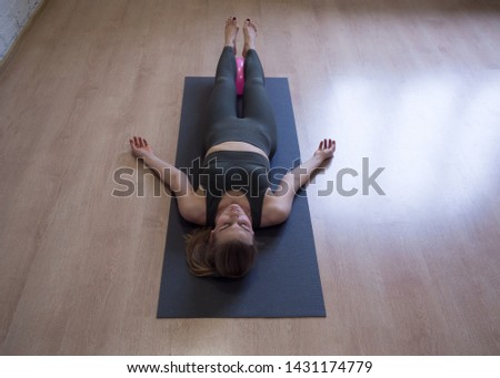 Woman laying on gray mat in relaxing pose on the floor, front view, yoga class. Fitness, routine, nidra, smart body, rest, meditation, tranquility and deep breathing concept Royalty-Free Stock Photo #1431174779