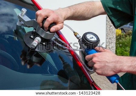 Glazier repairing windshield on a car after stone-chipping damage Royalty-Free Stock Photo #143123428