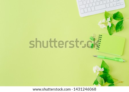 Flat lay blogger or freelancer workspace with a notebook, keyboard, jasmine flowers and green leaves on a green background
