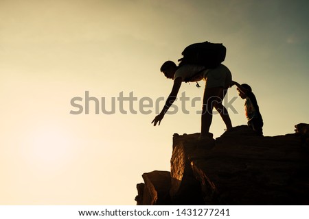 Silhouette hiking mother woman and kid on top hill summit giving hand to help other climbers during sunset. female mother hike to mountain peak. Family activity of outdoor sport and helping concept.