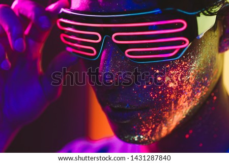 Handsome boy dancing at the rave party with fluorescent paintings on his face Royalty-Free Stock Photo #1431287840