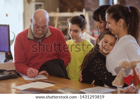 View from side of big family standing at reception and booking apartment for holidays. Old grandfather signing documents while children standing near and smiling. Concept of reservation.