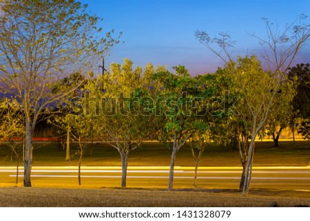 Night picture with light trails of cars on a road in Palmas City, Tocantins, Brazil. Green trees and sky with intense tones of blue, lavender and purple. 2017