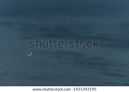 Crescent moon in cloudy sky at blue hour.