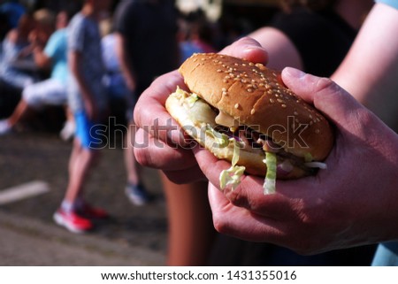 Burger on street food festival in hand. Pulled pork or burger are sold on Open kitchen food festival event. Street food in food stall.