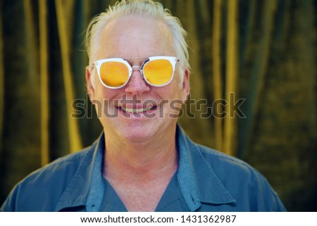 Man in a photo booth. A handsome man wears Gold Hipster Sunglasses while in a photo booth with gold velvet drapes. 