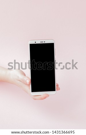 Modern mobile phone in a woman's hand on pink background.