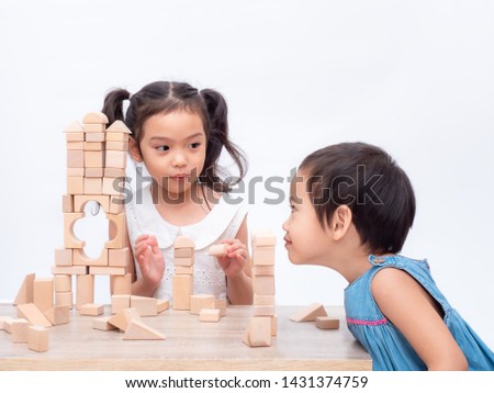 Two little cute girls are playing wooden block on wooden table and white background. Younger sister learning how to play block from older sister. Blocking is supplement child's development.