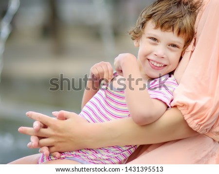 Close-up portrait of beautiful disabled girl in the arms of his mother having fun in fountain of public park at sunny summer day. Child cerebral palsy. Inclusion. Royalty-Free Stock Photo #1431395513