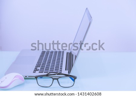 computer laptop with mouse and glasses on glass surface table and white background