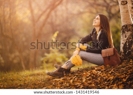 Beautiful young woman sits in autumn forest in yellow blouse with maple leaves and enjoys life. Freedom concept.
