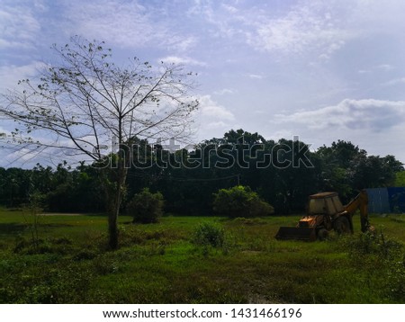 Old village road with leafless tree and farm with cloudy skies with a muddy old tractor and Backhoe loader