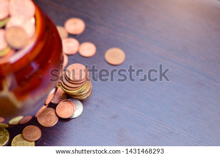 Many coins are in the jar. And spread beside