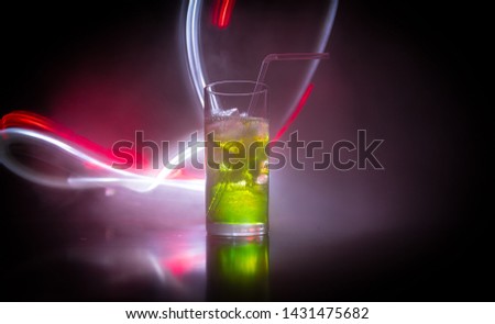 Cocktail glass splashing on dark toned smoky background or colorful cocktail in glass. Party club entertainment. Mixed light. Selective focus