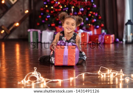 Little black girl oppening gift box, wearing beautiful dress, studio shot.