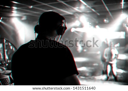 DJ mixes music in a nightclub with people dancing on the dance floor. Black and white photo with glitch effect and small grain