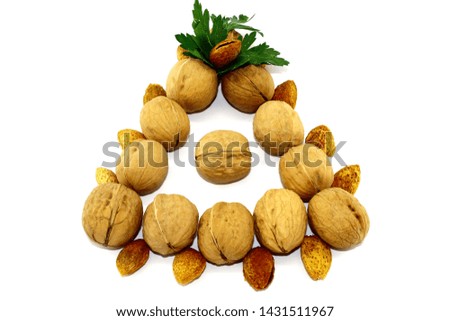 Walnuts and almonds form a triangle on a white background, there is also a small parsley leaf
