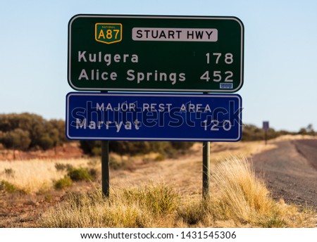 A roadside highway sign with distances to Kulgera and Alice Springs and then the next major rest area along the Stuart Highway in Marryat.