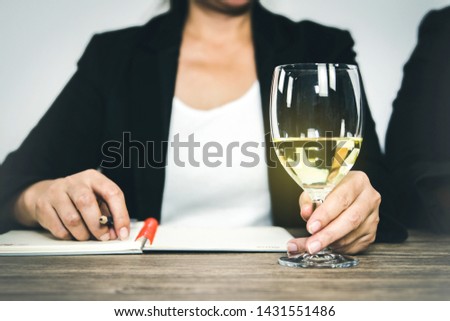 Sommelier, expert woman inspecting alcoholic beverages, white wine and taking notes on the test of the flavor of the wine
