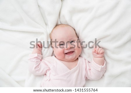 Newborn baby girl posed on her back, on blanket of fur, smiling looking at camera