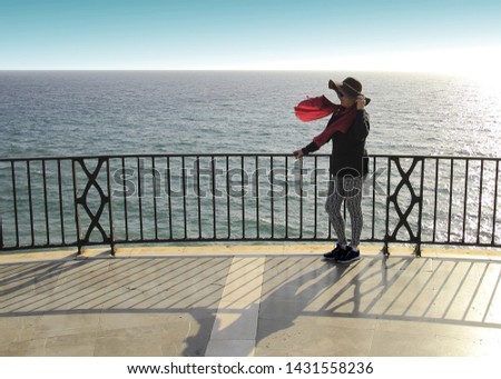 Perched by the sea of mature woman with hat and pants, photograph of a tourist in the viewpoint of the balcony of Europe, Nerja, Málaga, Andalusia, Spain, Woman, girl, are hat, pamela, wind,