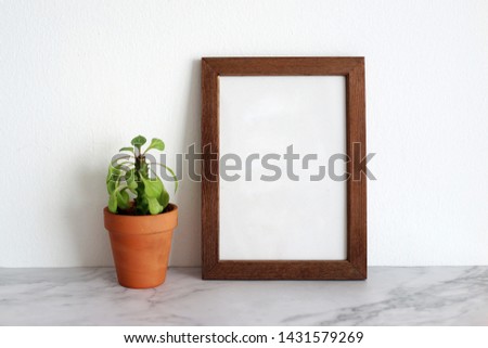 Blank wooden picture frame for copy space. Minimal interior decoration concept with green potted plant on desk.