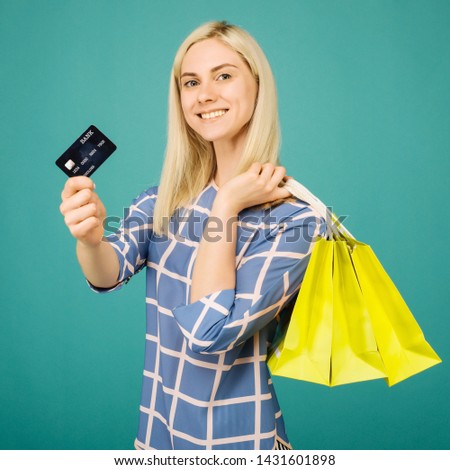 Happy girl in a checkered blouse holds credit card and shopping bags on blue background