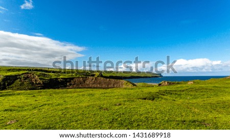 Green Irish meadow landscape next to Doolin Bay with the cliff in the background, sunny day with a blue sky with white spring clouds on a calm day in County Clare in Ireland. Wild Atlantic Way