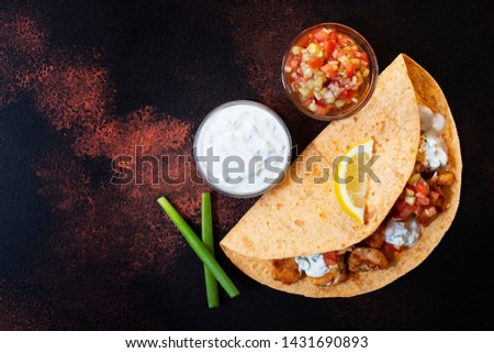 Traditional Mexican fajitas with chicken and vegetables, served in tortilla with white and red sauce, lemon and fresh green onions. Top view. dark background. Copy space