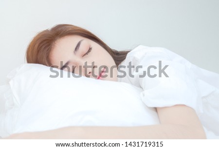 Beautiful woman sleeping in the bedroom.
Woman lying face down on the bed.Girl wearing a pajama sleep on a bed in a white room in the morning.Warm tone.Do not focus on the main object of this image.