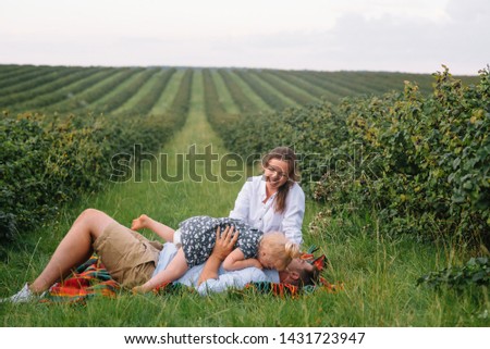 The daughter hugging parents on nature. Mom, dad and girl toddler, walk in the grass. Happy young family spending time together, outside, on vacation, outdoors. The concept of family holiday.