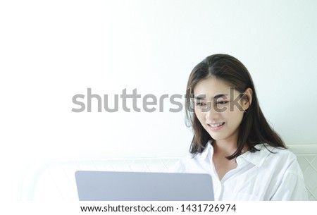 Beautiful Asian woman is smiling.Lady work with laptops on the sofa in the room in the morning.She is happy to get a new job, success, or get good news.Do not focus on the main object of this image.