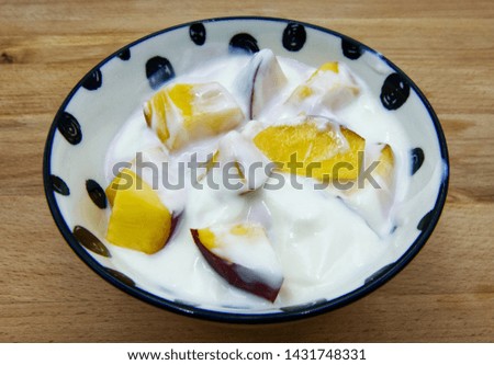 Yogurt in a bowl with peach slices on wooden background