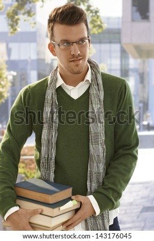 Outdoor portrait of male student holding books outdoors.