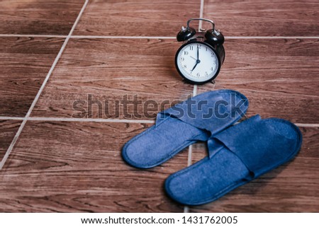 Blue Slippers and alarm clock. Bedtime. The view from the top. Conceptual image for waking up in the morning and good morning. Slippers and alarm clock on the wooden floor.