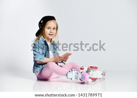 Preatty girl sitting in roller skates, wearing a blue denim and cap and smiling. 