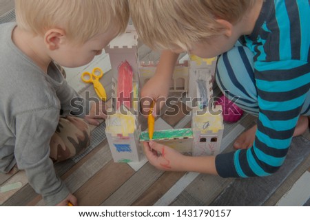Happy boys build vintage cardboard castle and draw it with felt-tip pens. Children are happy together on holiday. Game and intensive learning of preschoolers. Shallow focus.