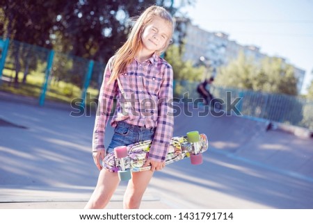 portrait of a beautiful little teenage girl, holding in hand skateboard, in skatepark. on the background rolling around boy on bike