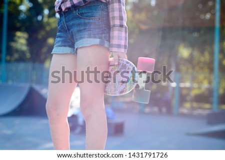 teenage girl holds in hands color skateboard, in a beautiful sunshine