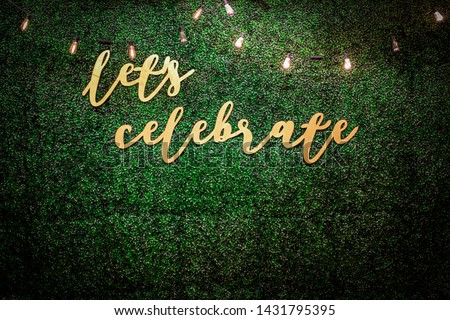 “Let’s Celebrate” lettering on a dark green leaf wall.
