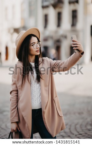 Attractive young woman wearing coat sitting outdoors, taking a selfie
