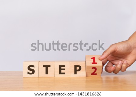Hand flip wooden cube with the word STEP 1 to STEP 2 on white background. Business concept Royalty-Free Stock Photo #1431816626