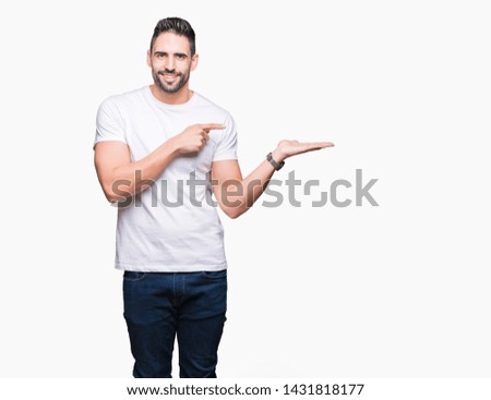 Young man wearing casual white t-shirt over isolated background amazed and smiling to the camera while presenting with hand and pointing with finger.